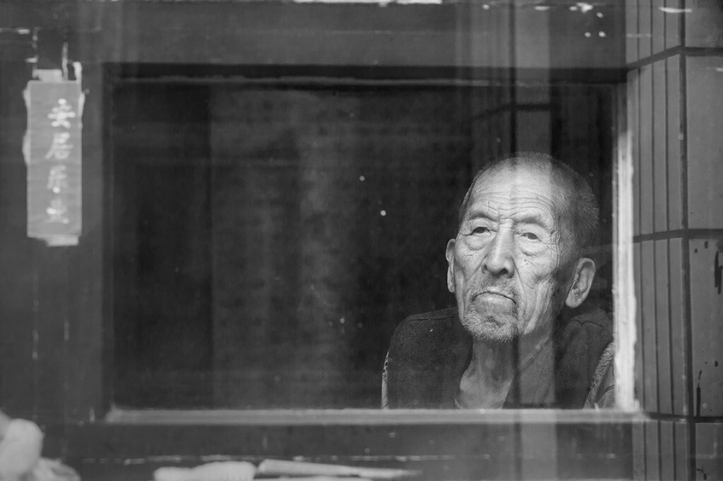 老人靠窗在祈盼着什么,村里基本上都是独居老人,子女们都外出务工.