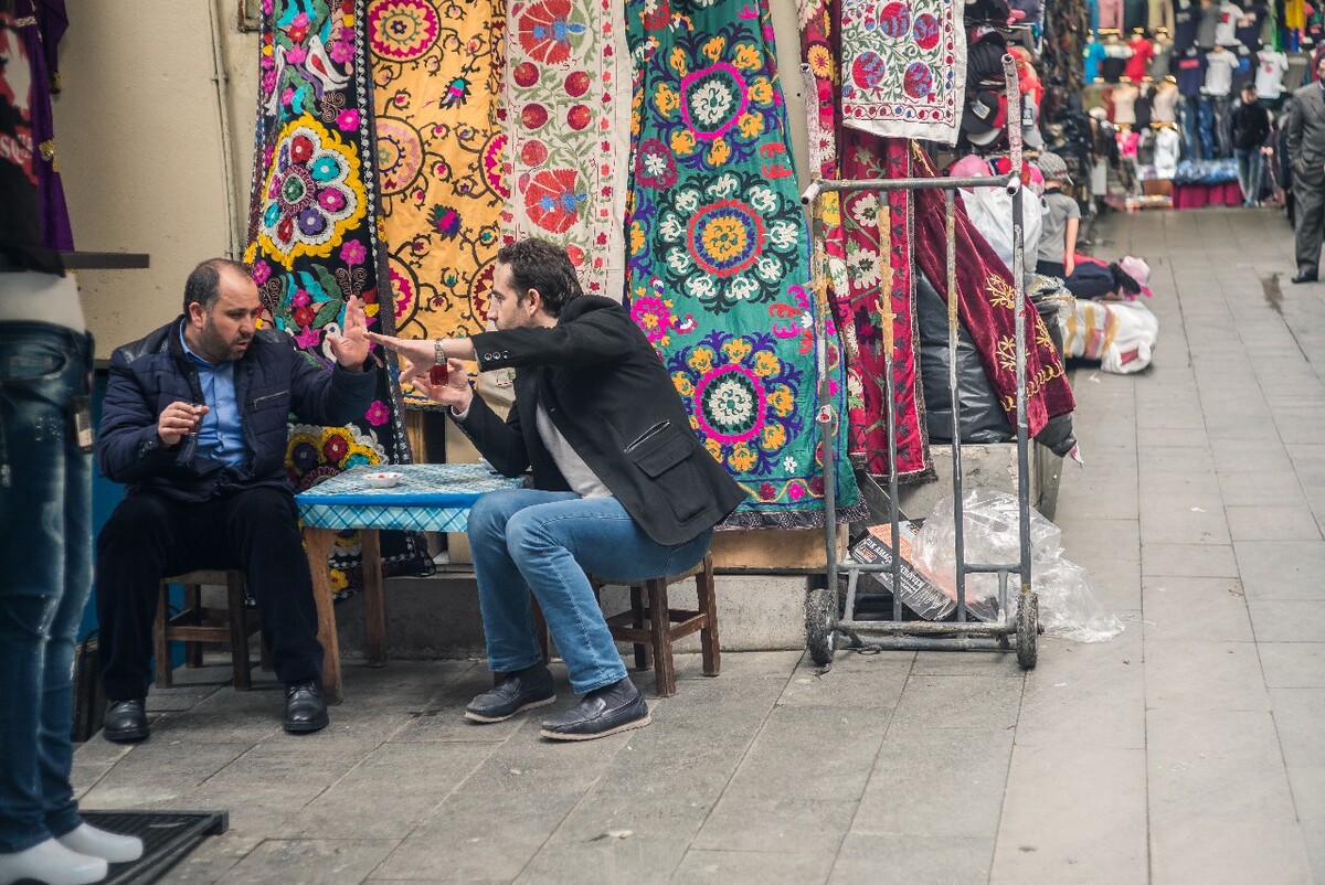 两个卖纺织布料和衣服的老板坐在一起聊生意、喝茶。