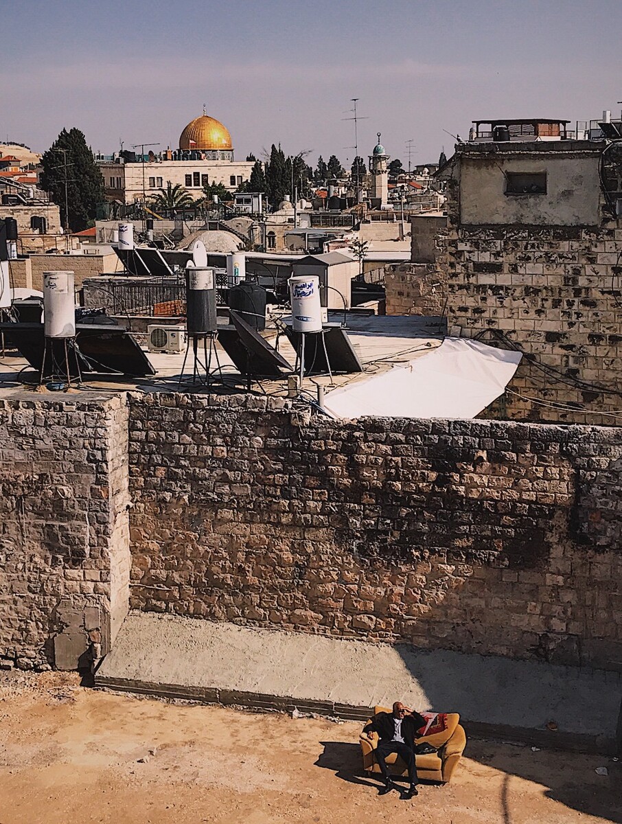 在耶路撒冷老城城墙上遥望穆斯林区的金顶圣殿。眼前的一片空地上，默然立着一张沙发，一个老人坐在上面晒着太阳四处张望，遗世独立，在神圣气氛笼罩的小城墙下，老人好似逍遥于世外。