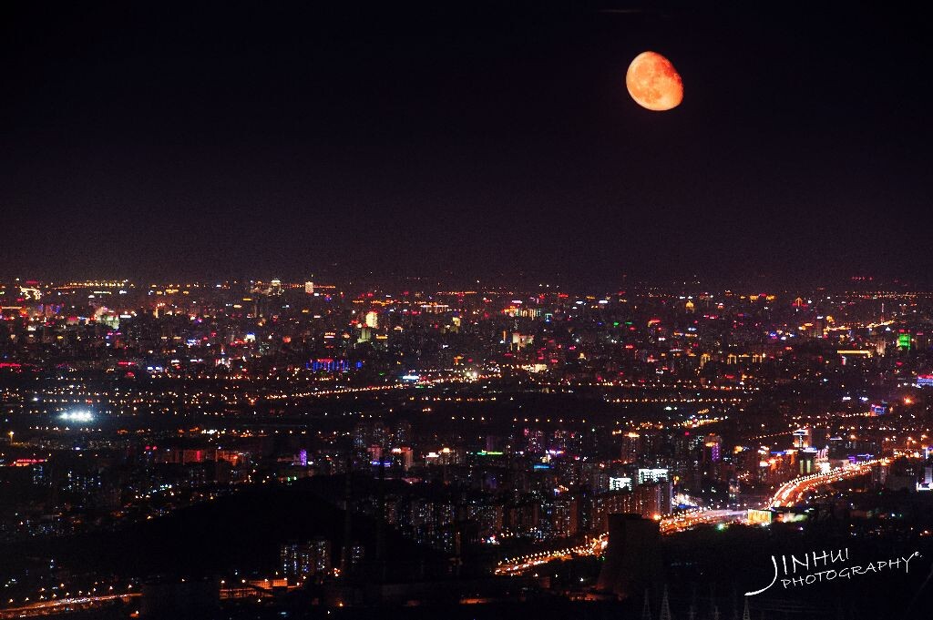 红月亮从地平线缓缓升起，遥望城市夜景