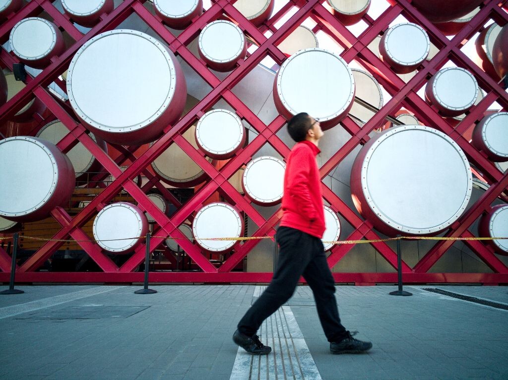 行走街头2——仰望。奥林匹克公园下沉广场，一个为扶梯设计的中国红色大鼓外墙。一个身穿红色衣服的人正好路过这里，仰望这面鼓墙
