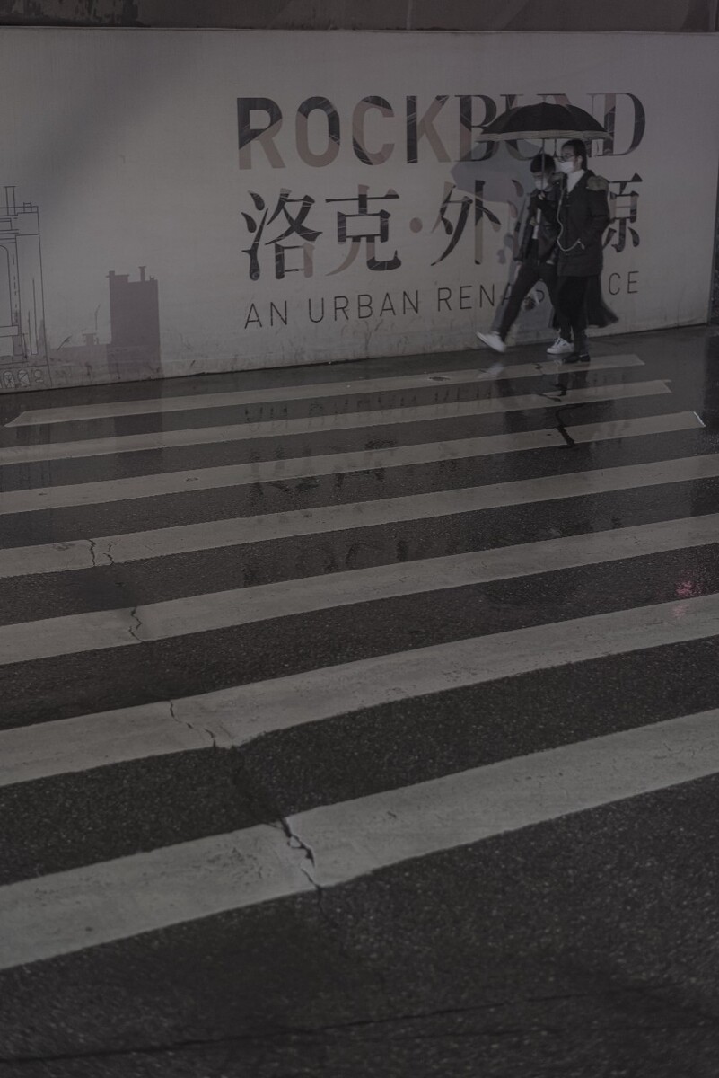 雨中，一对年轻人撑伞走过广告牌。