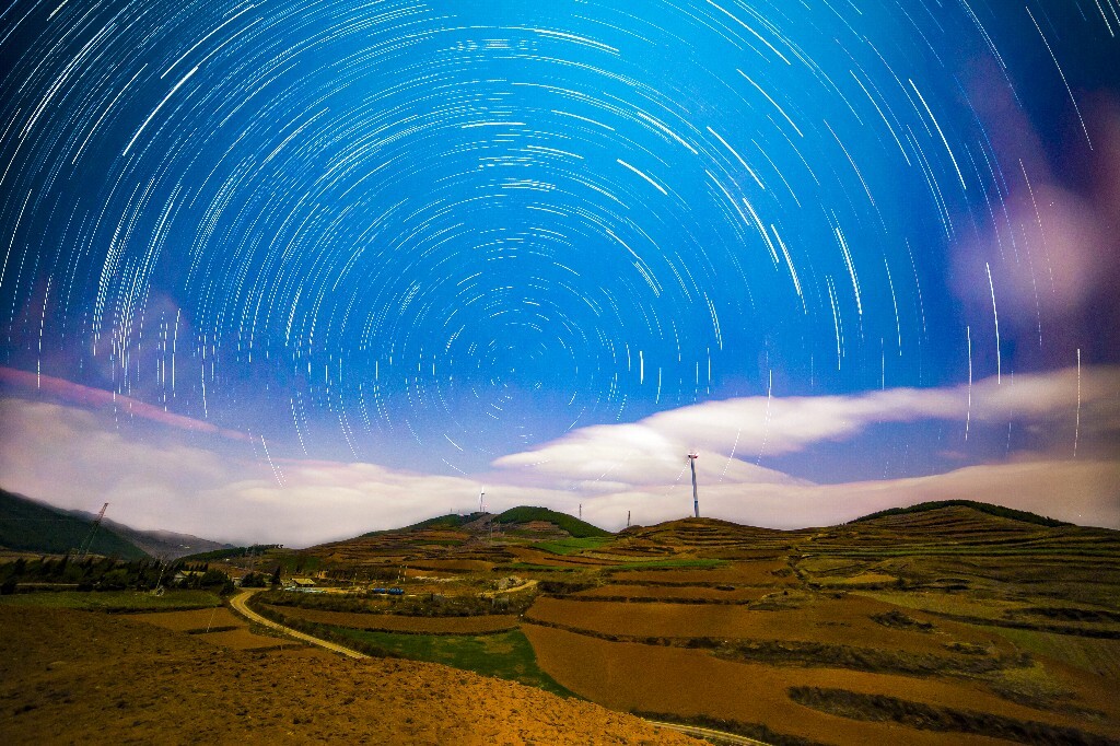 东川红土地在月光的照射下亮如白昼，漫天的星点随着风车在旋转。