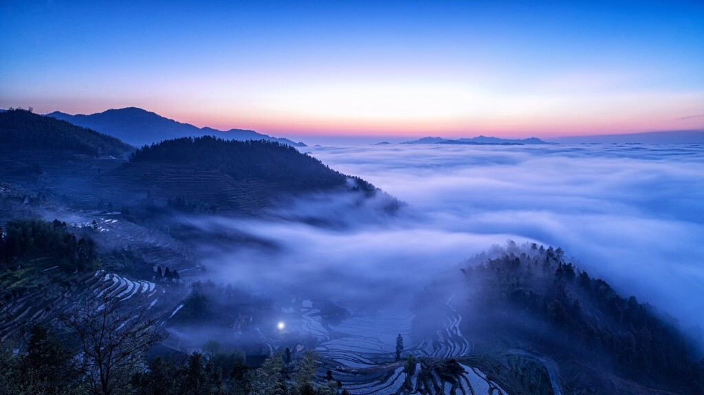 太阳即将升起，妙曼的云雾漫进了宁静的村庄，早起的村民点亮了家门口的灯光，准备着一天的生计。站在山坡上的我，陶醉在这美丽的画卷中。