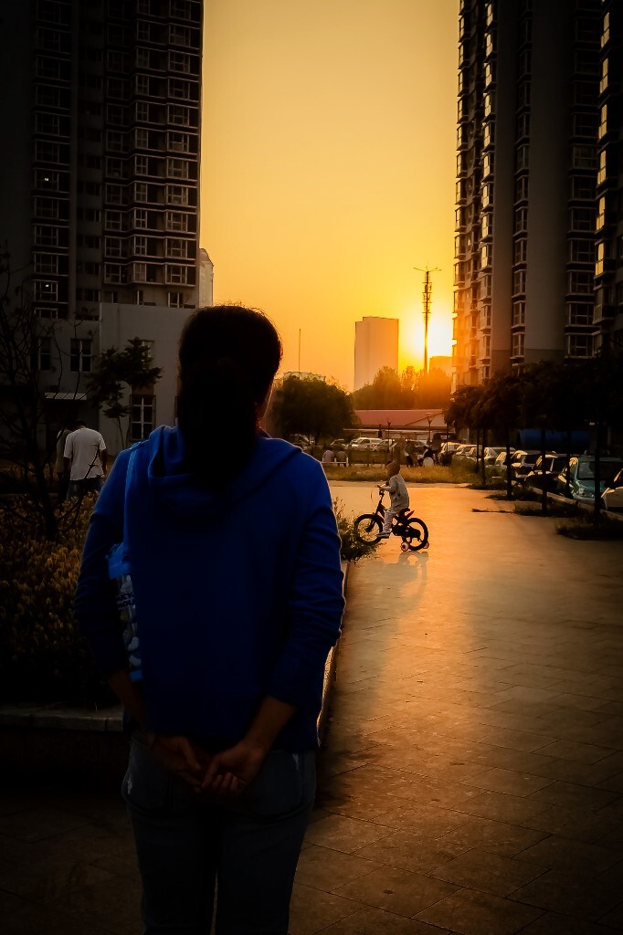 一位母亲远远的望着骑自行车的孩子，想让他独自前行又怕他摔倒