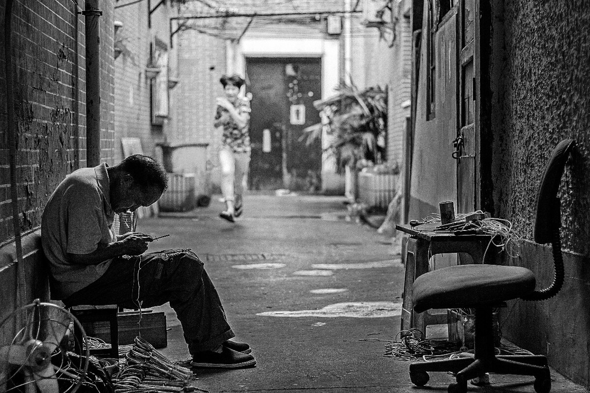 他低着头弯着腰，端正地坐在小矮凳上，认真做着手工。不远处奔跑撒欢的小孩，对他丝毫没有影响。也许他就依靠卖这些手工维持生计，虽然看上去值不了多少钱。这张岁月斑驳的脸，曾经坎坷，曾经年少。