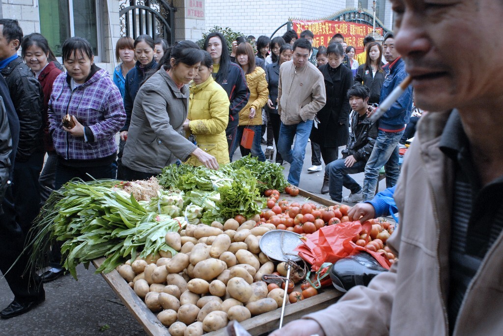 11.	2012年3月10日，广东省东莞市。打工者们下班后，在工厂大门前的流动菜摊前买菜。