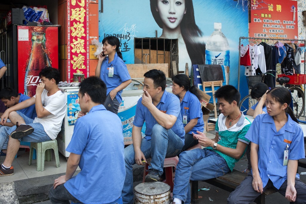 19.	2013年5月13日，广东省东莞市。打工者们吃过晚饭后，在工厂外的杂货店看电视，然后再加班至晚上九点钟以后。