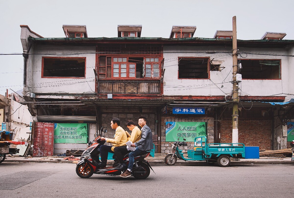 2016年4月2日，上海，一辆载满了年轻职员的电动车，从拆迁的老弄堂里飞驰而过。