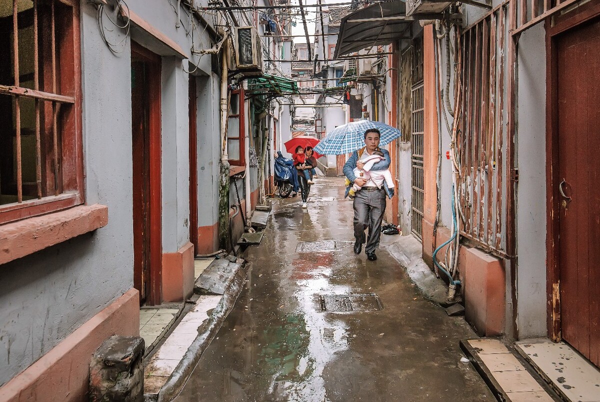 2016年4月3日，上海，大雨中，一对年轻的夫妇抱着孩子穿梭在弄堂间赶路的情景。