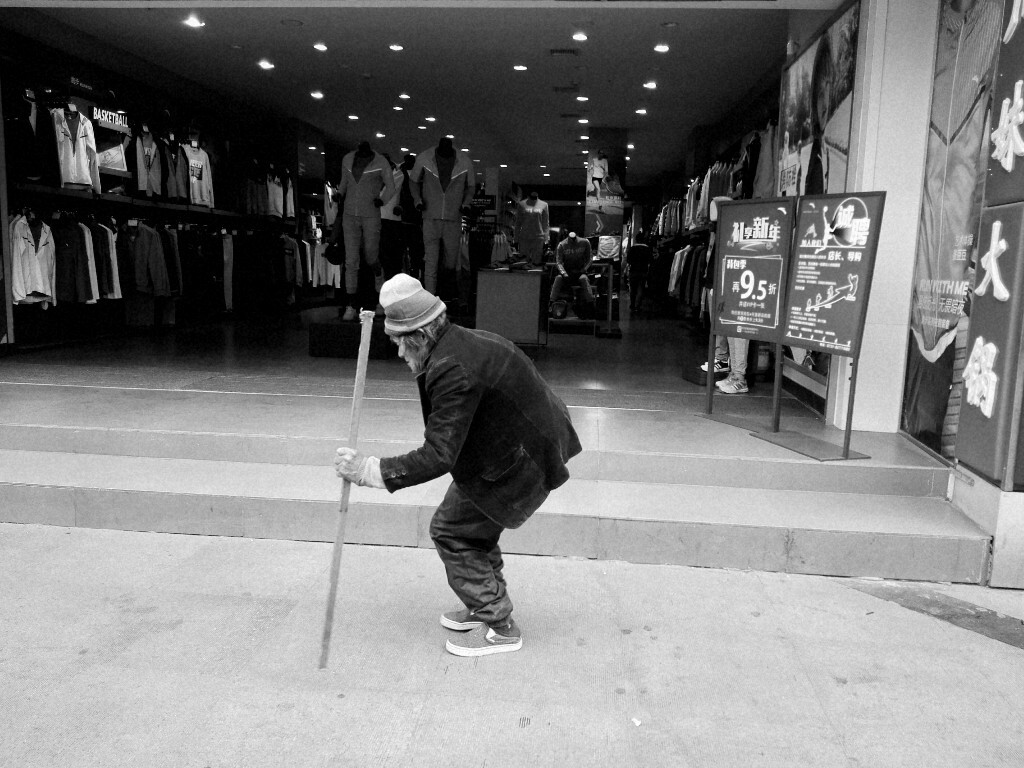 老人家拄着棍子走过一家服装店.