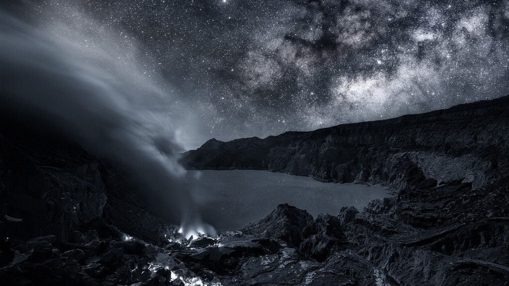 Ijen 火山坑银河<br />
<br />
宜珍Ijen火山是位于印度尼西亚爪哇东端的一座活火山。有著名的“蓝色火焰”以及喷着浓烟的硫磺矿,还有绿蓝色的火口湖。<br />
<br />
半夜12点起床匆忙收拾妥当上车向宜珍火山出发,大约经过2h的颠簸到达山脚下的入口开始登山。从山下登顶大约有3公里的山路,出发时海拔1500多米,山顶2500米左右。一路爬上来,硫磺的味道越来越浓。在半山腰的时候租了防毒面具,才算缓和一些。<br />
<br />
经过2个多小时的攀登终于上到火山口,浓烟滚滚从山口底部飘拂上来四周围充满刺鼻的硫磺味道。火山口是个巨大的坑,隐隐约约看到下面绿蓝色的火口湖,下面飘上来的硫磺浓烟顺风飘。爬到山口,还得继续下到里面。。。底下没有“路”,都是陡峭的岩石。<br />
<br />
湖边上的岩石上到处都是黄色的硫磺,硫磺是硫酸制品的自然原料,被广泛用于石油提炼、洗涤剂和化肥当中。<br />
<br />
宜珍火山这个独特的火口湖,从这里火山喷出数以吨计的二氧化硫气体,岩浆里喷出的气体具有极强的酸性,所以湖水的酸碱度高的惊人,湖水PH值为0.5这是的蓄电池的酸液的3倍。遇到这个火口湖或者火山周围的气体,大多数东西都会烂掉金属也会腐蚀,酸度实在是太强了,湖水不仅酸度强而且还很烫,只有火山内部有非同寻常的惊人能力传递到地表时才能使水温高达43摄氏度,宜珍拥有地球上温度最高的酸性水体,在这个酸性湖泊岸边二氧化硫气体在埋进火山侧的管道里凝结下来,当地村民会采集沉淀下来纯硫磺块卖给制糖和日化企业。<br />
<br />
硫磺矿床近旁的人除了少量游客,就是采集天然硫磺的矿工。这是一项艰苦且危险的工作,矿工们在没有任何防护措施的情形下长期暴露于剧毒气体中。所采集的硫磺则要人工挑上山,再到三公里之外的山脚领取报酬。天色微明时,矿工们挑着沉重的担子开始回程,步履缓慢而坚实;从矿床到山顶的这七百多米是消耗体力最大的部分,剩下的三公里为平路或下坡,相信会好走些吧。