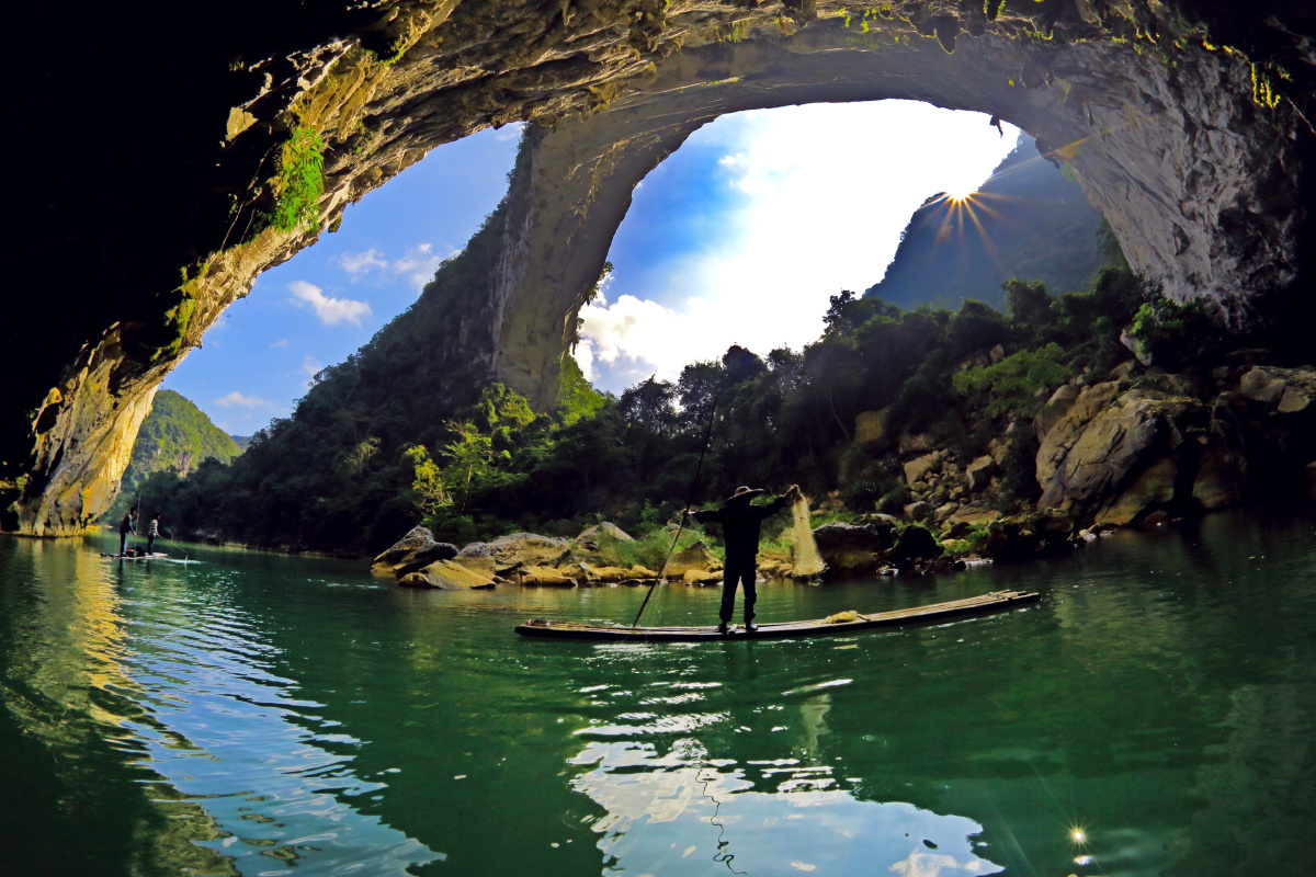 广西天峨县布柳河上仙人桥如一个天窗,太阳从窗外升起,窗下几个渔民在