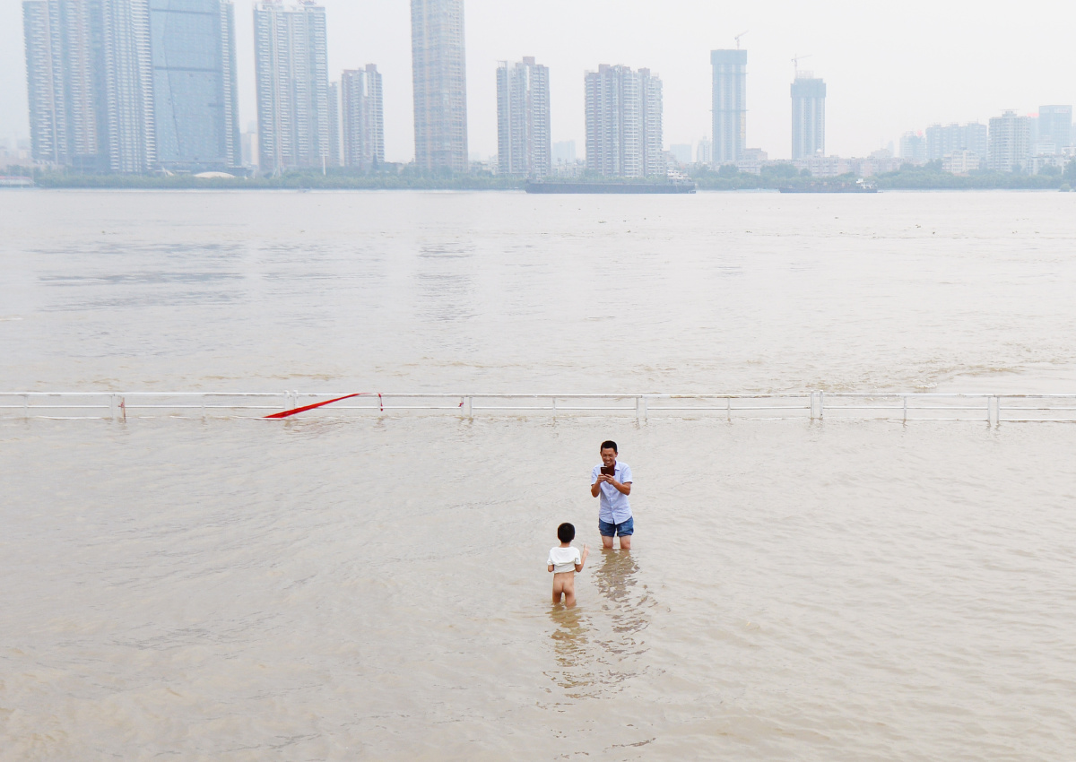 湖北省武汉市黄花矶码头,一位父亲站在江水中用手机给光着屁股的儿子