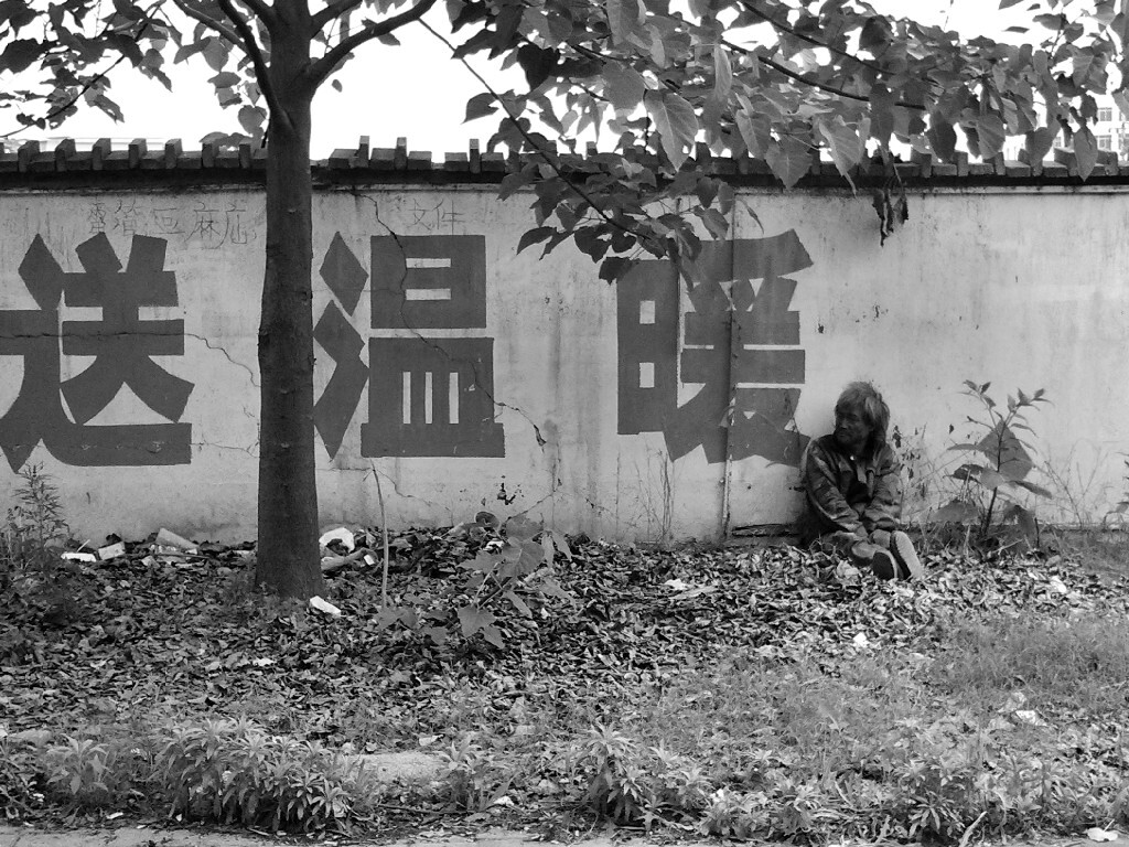 时间：2013年4月21日 AM<br />
地点：赣州 南康 灯饰城项目地<br />
过程：吃完早餐回售楼部的路上，看到这位流浪者依在围墙上晒太阳，“送温暖”这样的标语和流浪者的身份刚好形成强烈反差，瞬间觉得太TM幽默讽刺，拿起手机记录了这一刻。