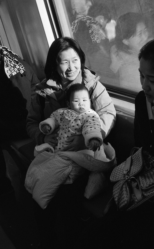 13号线城铁上遇到的可爱的小宝宝，她是一个小姑娘，是这位大姐的第二个小宝宝。为了让我拍照，大姐特地把她抱高了一点，太阳刚好能照在他们两人身上。我觉得很温暖。