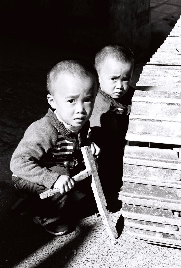 可爱的双胞胎小伙，在村镇的小路中间玩耍，他们貌似在研究挖掘机的履带机械原理。