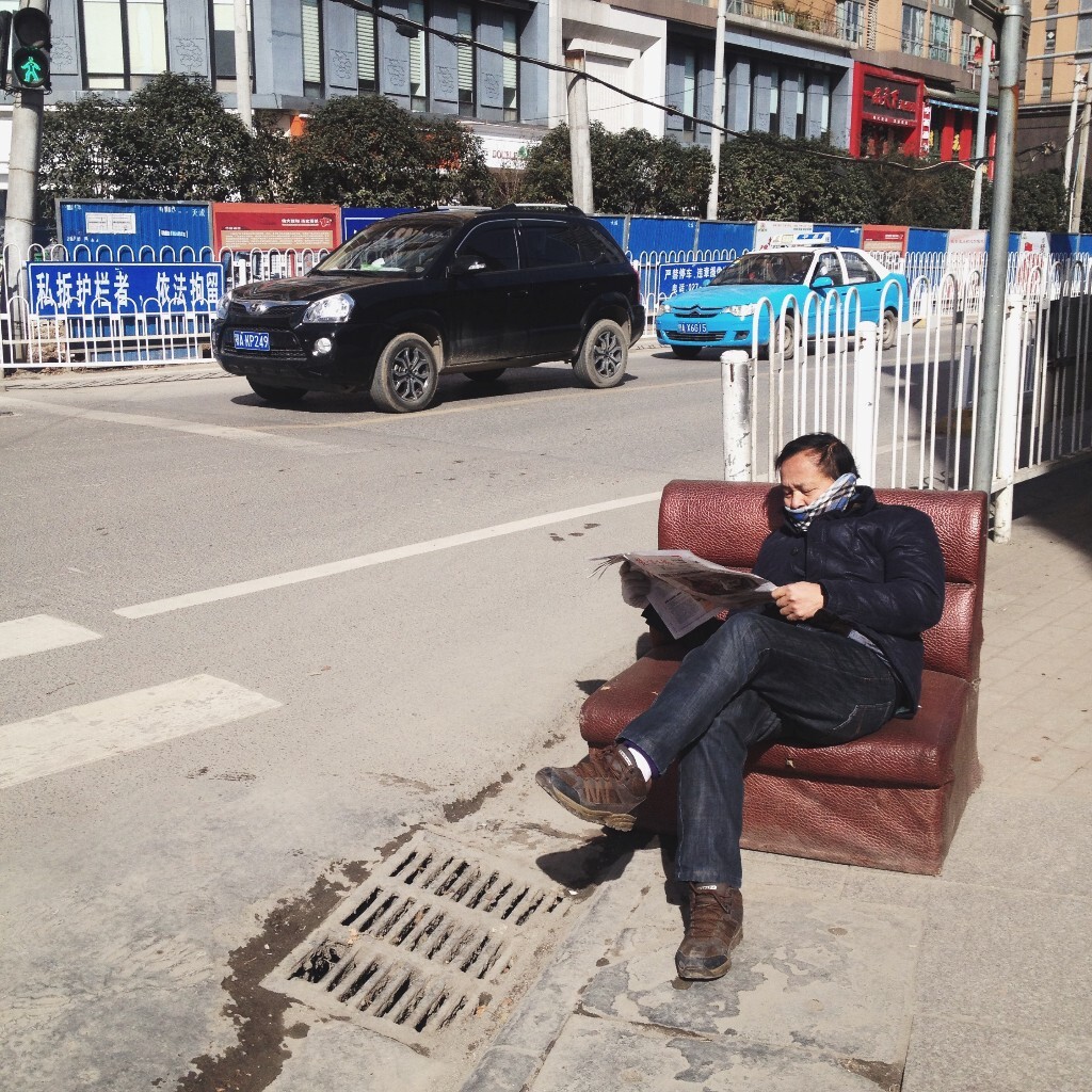 坐在路边沙发上看报的男子。