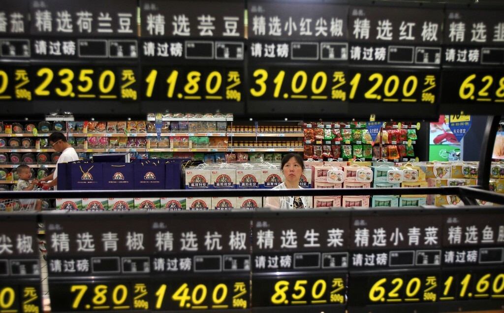 2013年8月9日,一位市民在满是价格标签的蔬菜销售柜台后面仔细查看蔬菜价格。<br />