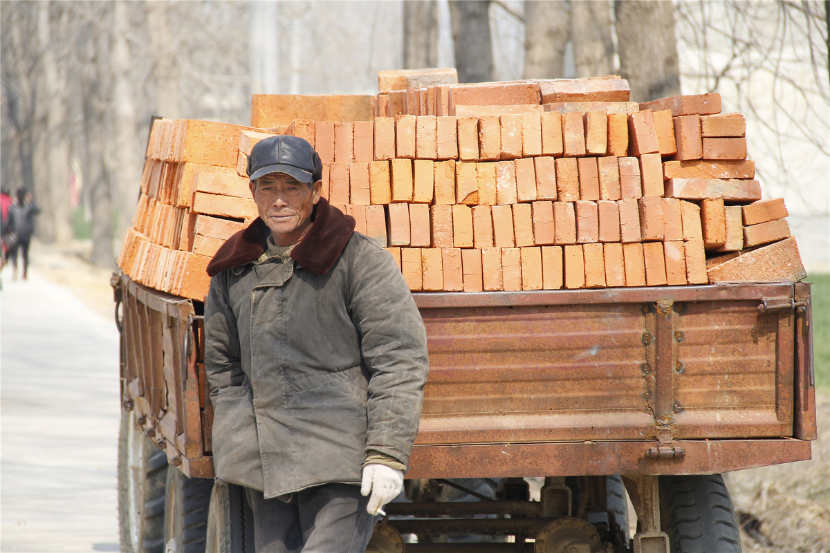 2016年2月9日,安徽阜阳行流镇乡村道路上,一位卖砖农民在路边等待生意