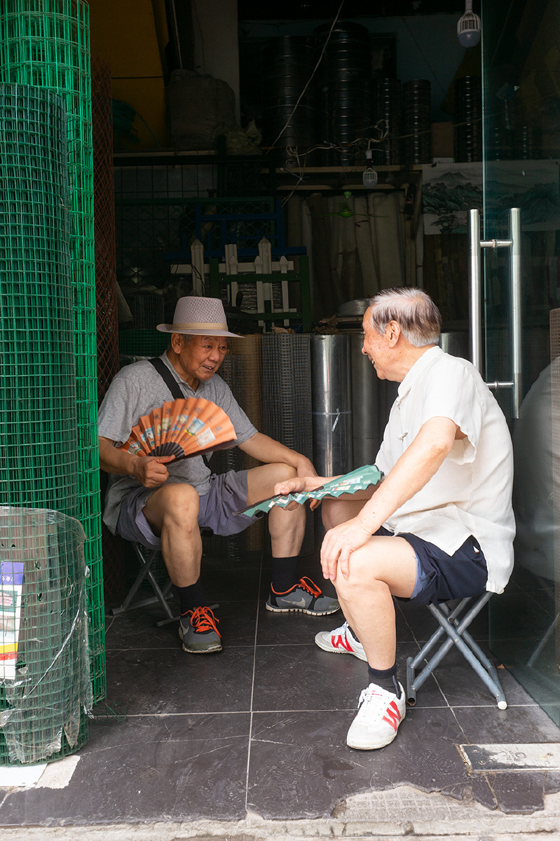 难耐馆驿街上老哥俩左80岁右76岁坐在店门口手摇扇子纳凉聊天谈的欢