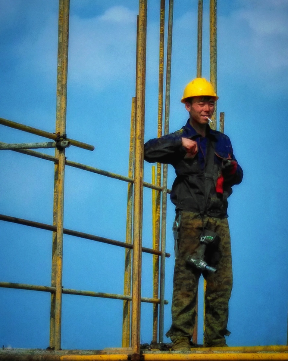 站在高空中艰苦工作的外架工人,休息间,点上一根烟,遥望着远方微笑