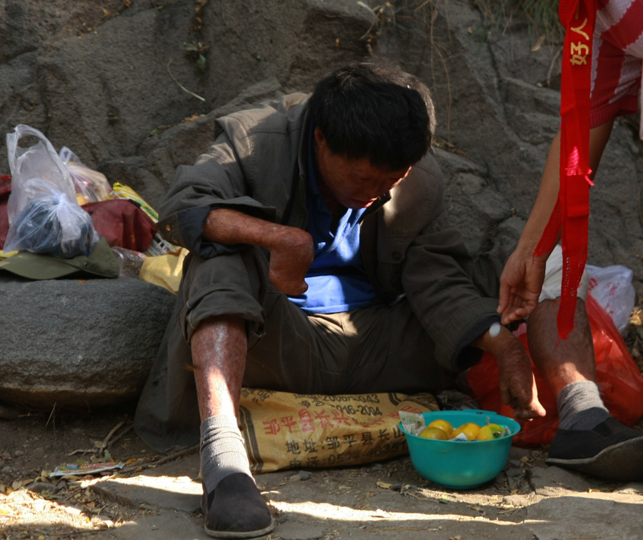 在一次庙会的路边一位游客弯腰向残疾人的盆子里放入一枚硬币  拍摄于