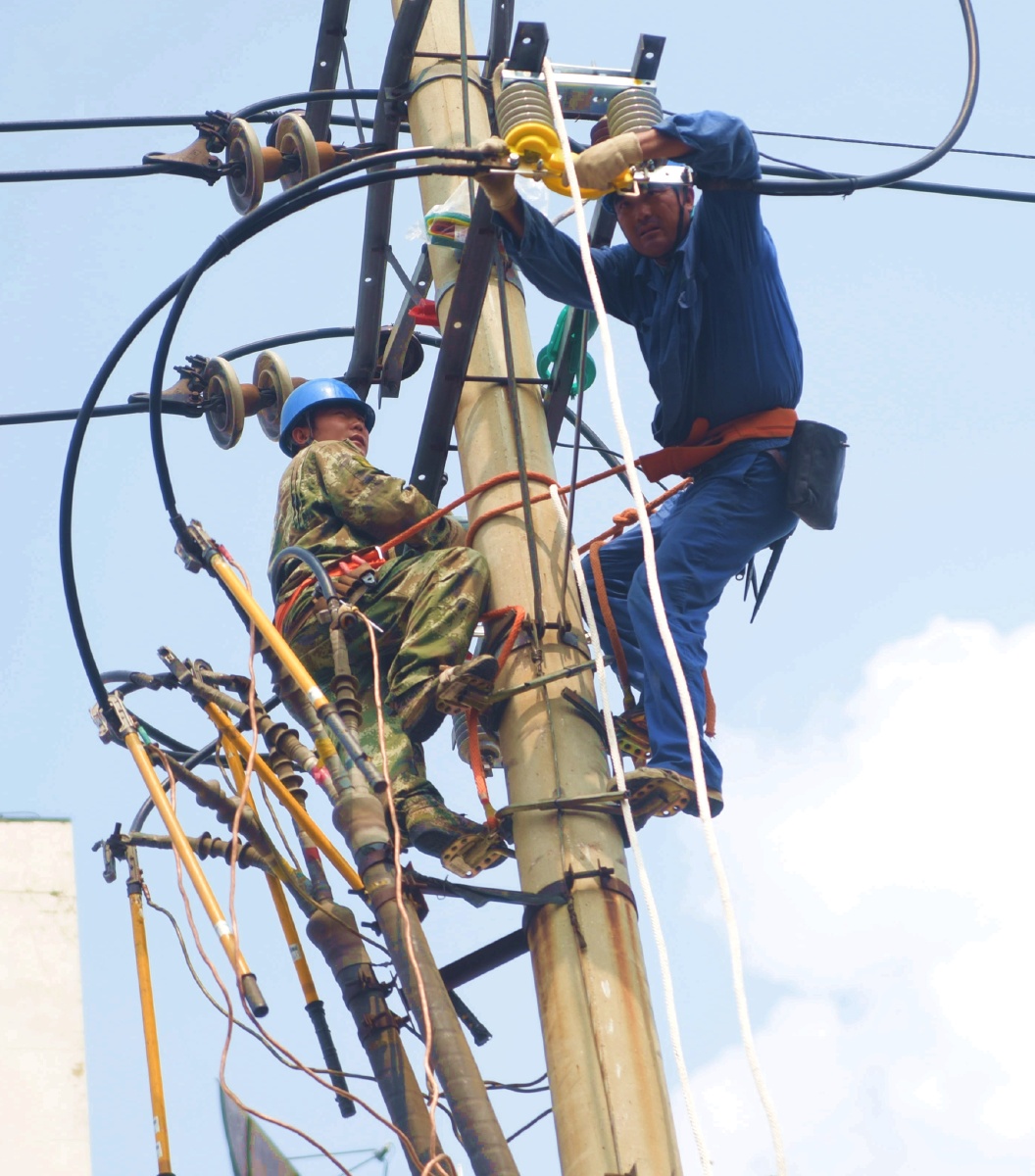 两个电力工人在检修电线,他们的工作服在天空里是美的色彩.