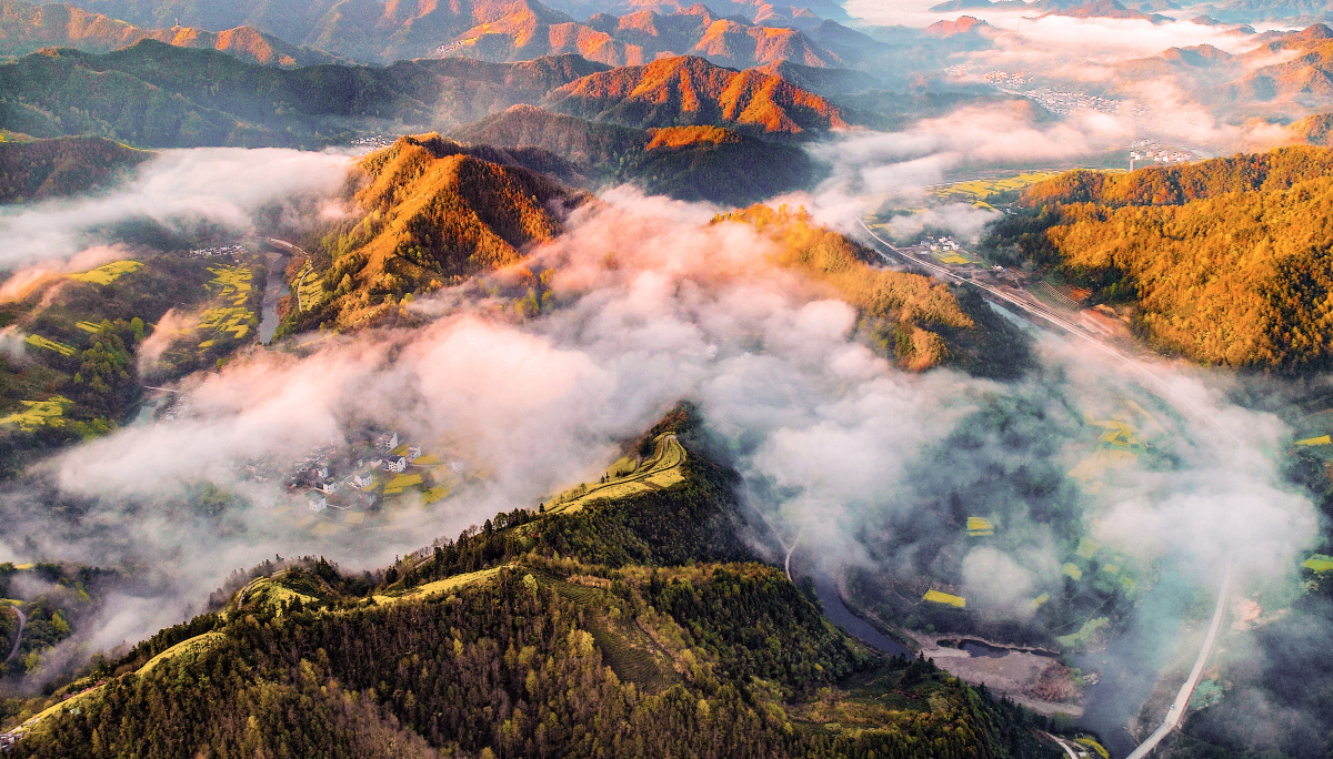 散落于山间的山村被晨雾笼罩,太阳出来,朝霞映红了山峦,白雾