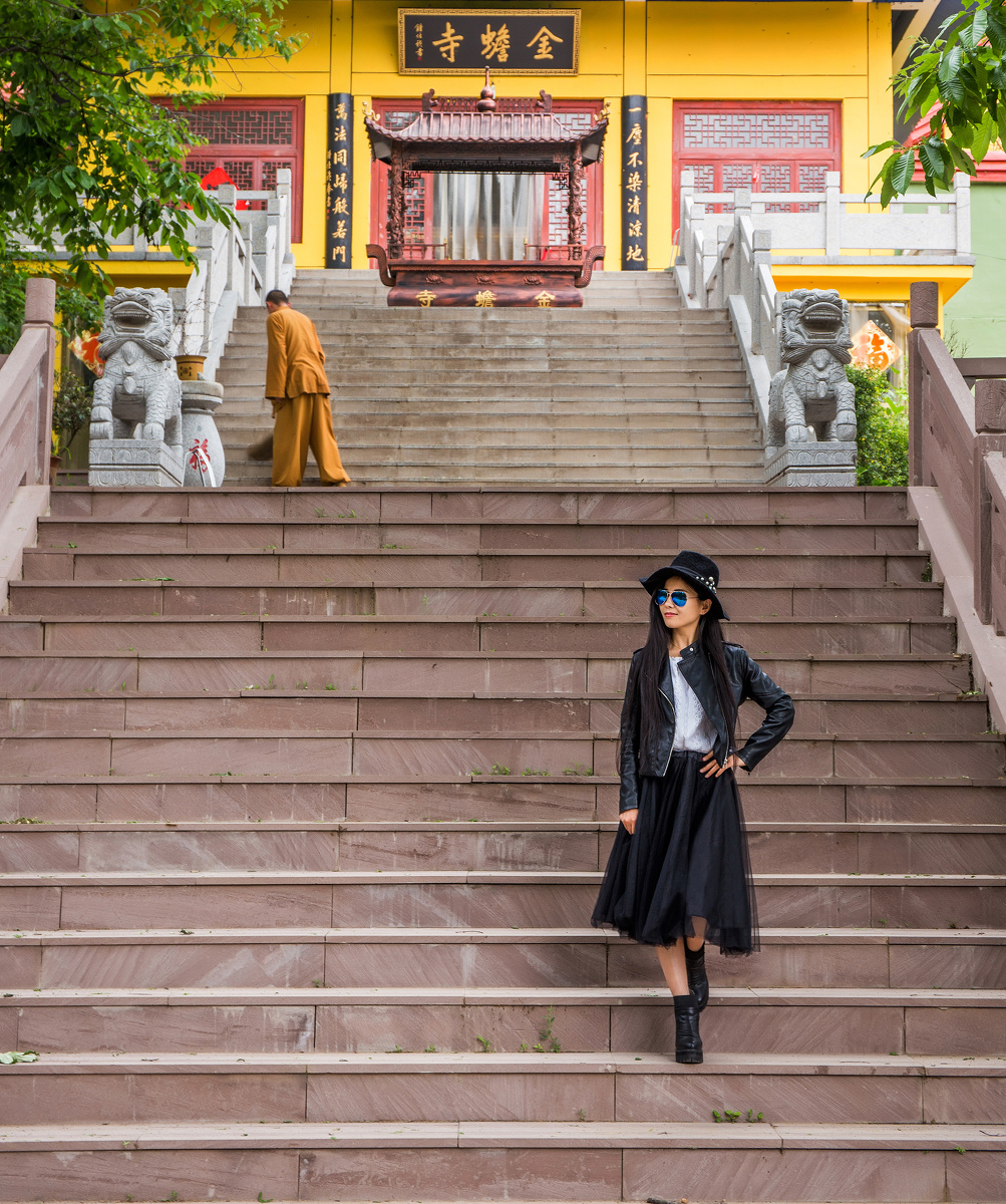 一位时髦的美女在小城公园的寺庙大殿前留影,与身后一心扫地的出家人