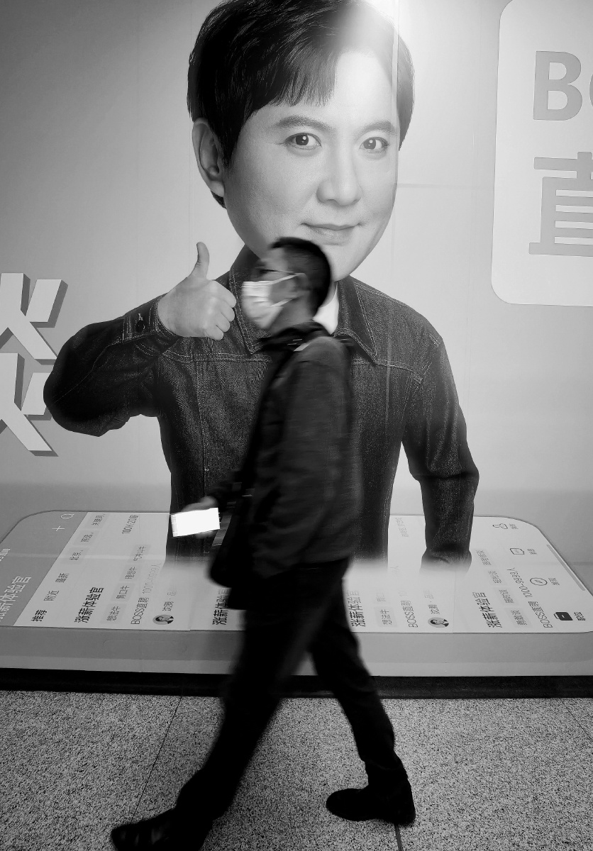 一张沈腾竖起大拇指的海报面前一个戴眼镜的男子匆匆走过