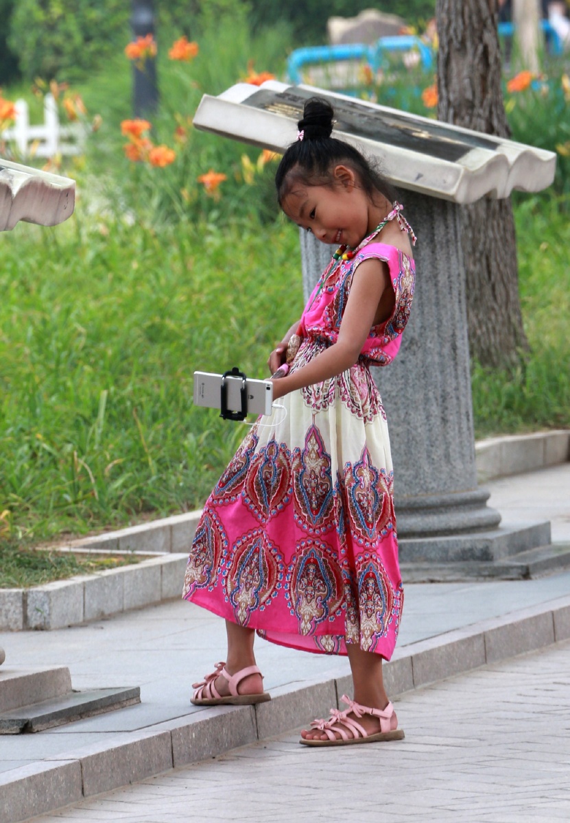 公园里,一位小女孩儿正在像模像样的自拍,好有情趣.