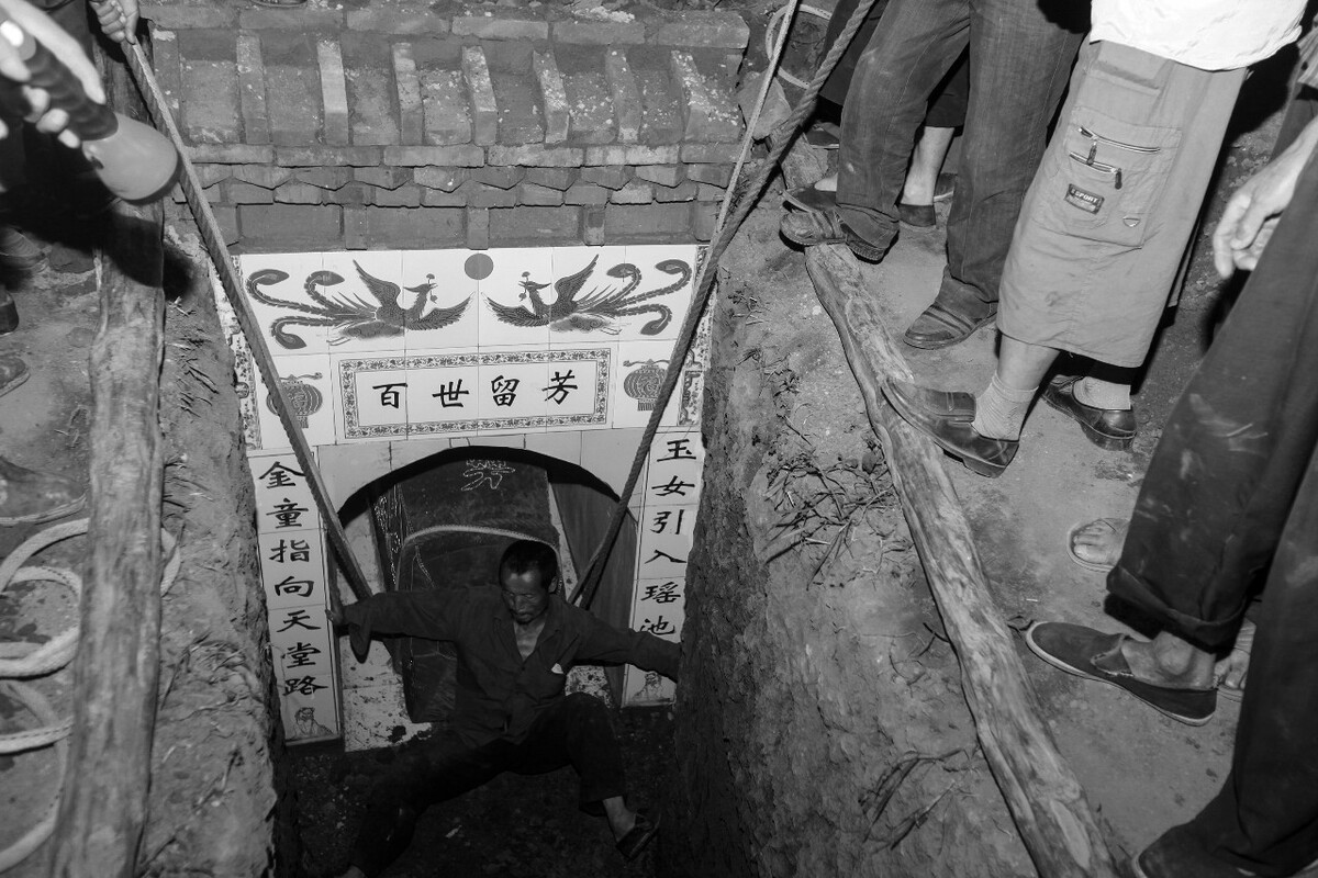2012年7月,陕西宝鸡,棺材送进墓道内,打墓的匠人背靠棺材,用脚蹬墓道将棺木送入墓室。关中农村经济条件略好点的人家,墓葬结构都是砖垬墓。这种墓葬无法用大型机械在地下作业,只能靠打墓的匠人在狭小空间内挥动小锄头,再将土一小袋一小袋装运出去。