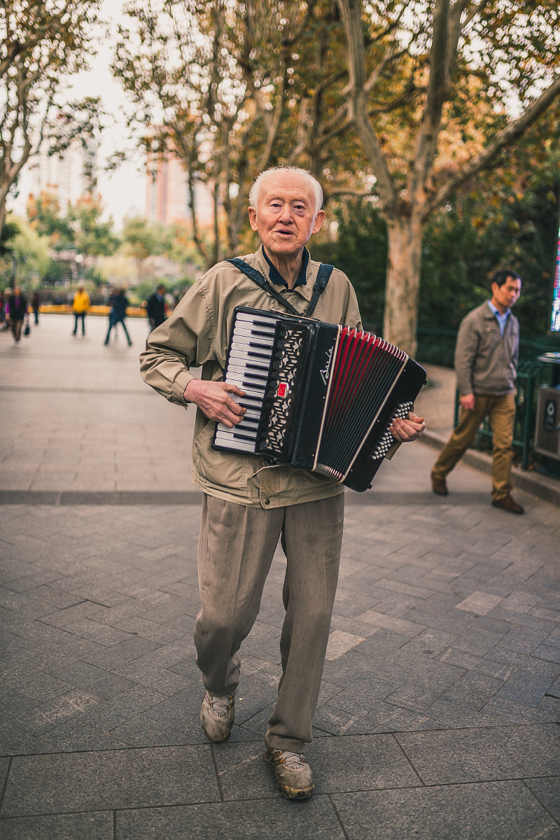 上海的秋天 大片的树叶散落在和平公园里 一位老人一边拉手风琴一边