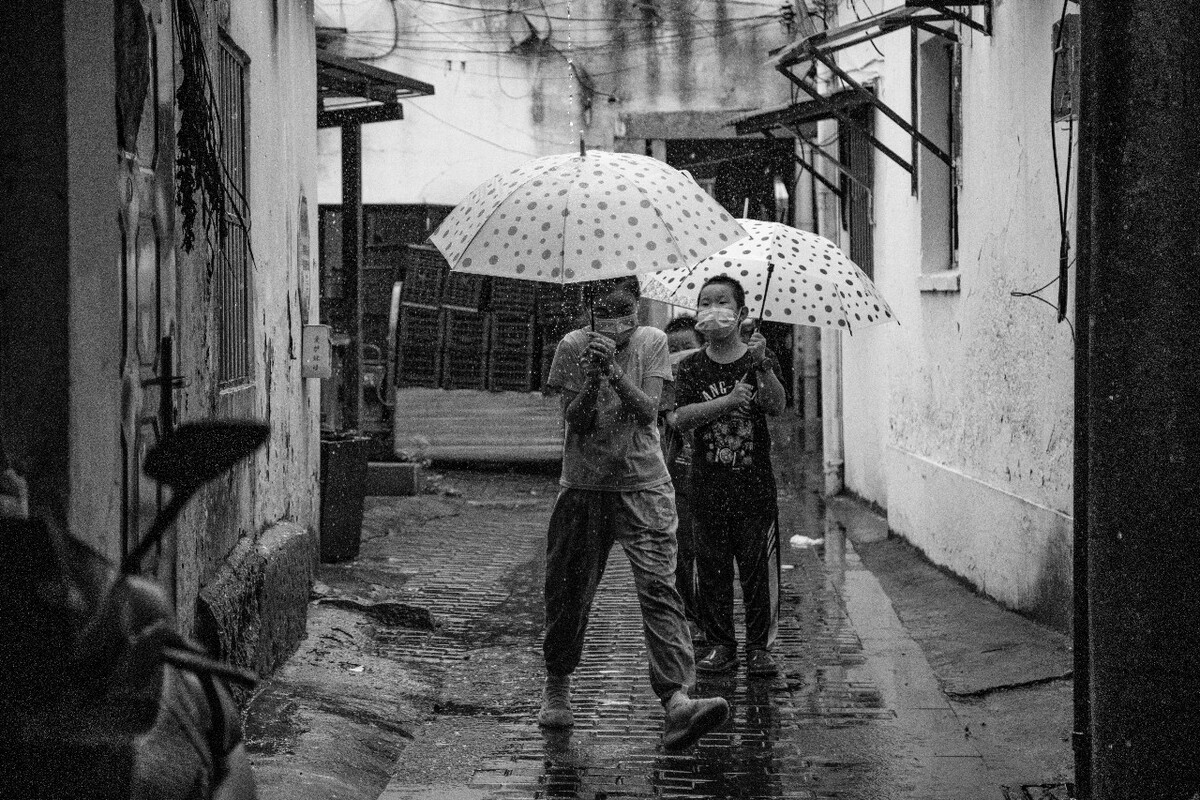 2021.08.13 苏州 山塘街所摄。三个和雨水陪伴着一起玩耍的小朋友,一个一个分别撑伞走过滴水的棚子。