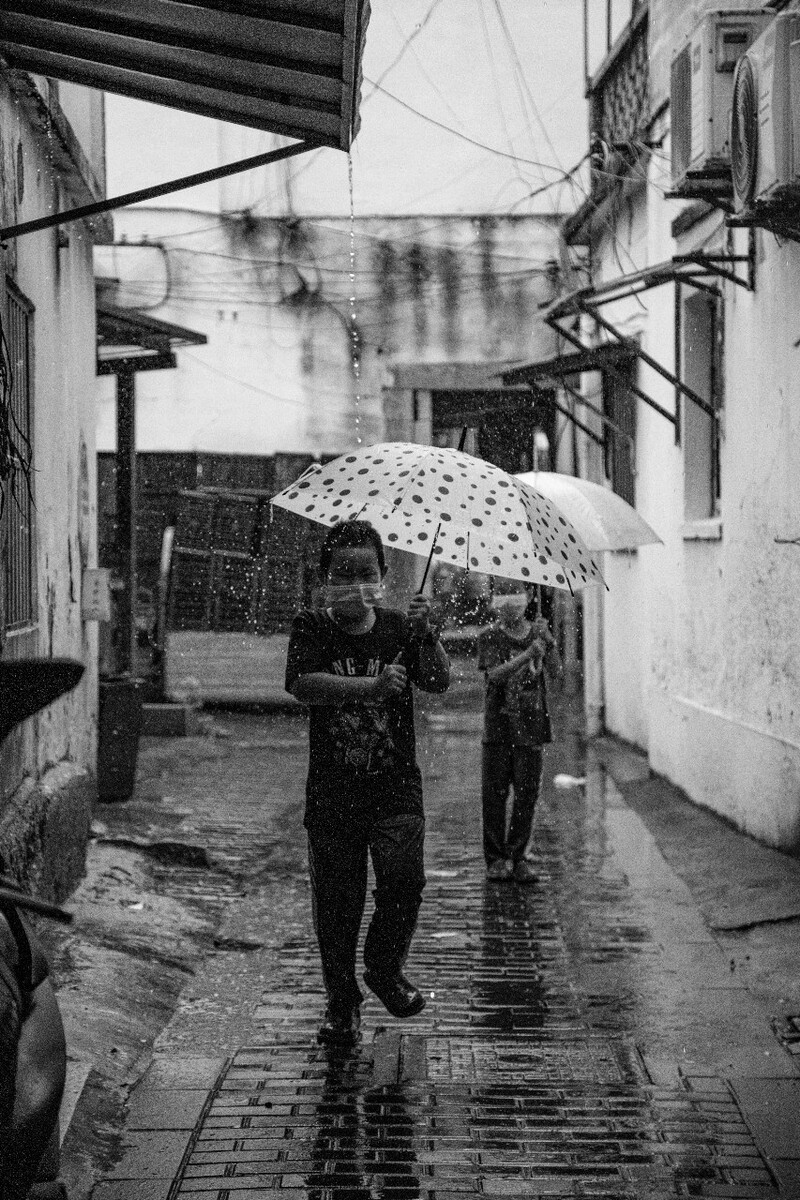 2021.08.13 苏州 山塘街所摄。三个和雨水陪伴着一起玩耍的小朋友,一个一个分别撑伞走过滴水的棚子。