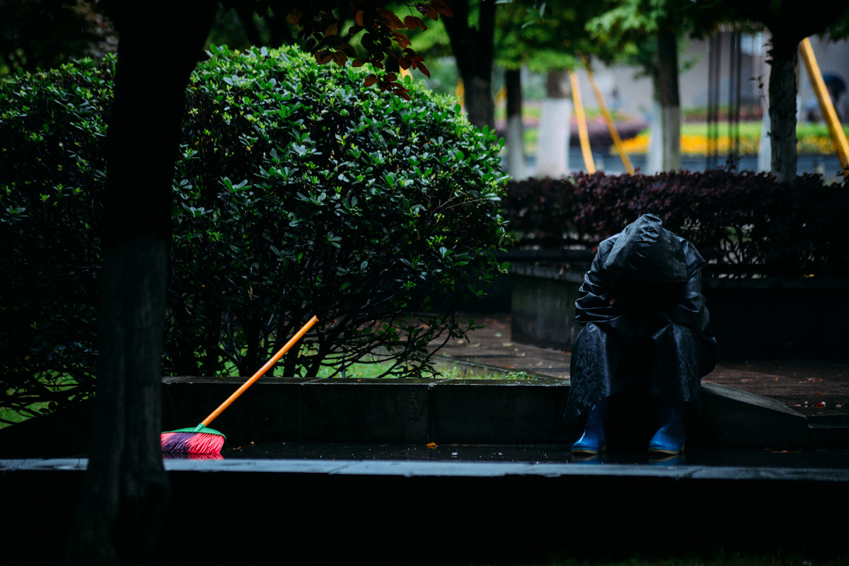 此时外面下着大雨,这名清洁工正在躲雨,穿着雨衣,坐在地上