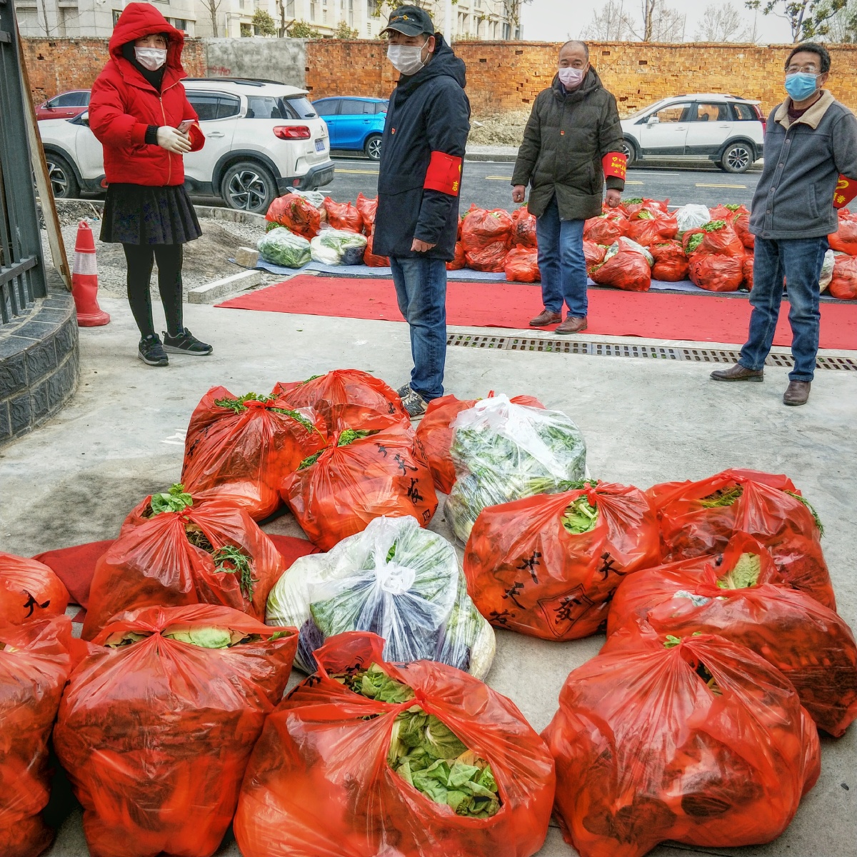 小区门口堆满了待分发的菜，每包25斤多，都是社区和志愿者们一包包卸下车的。