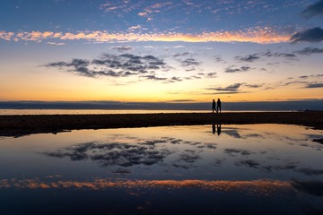 日落时分在海边散步的两人倒影