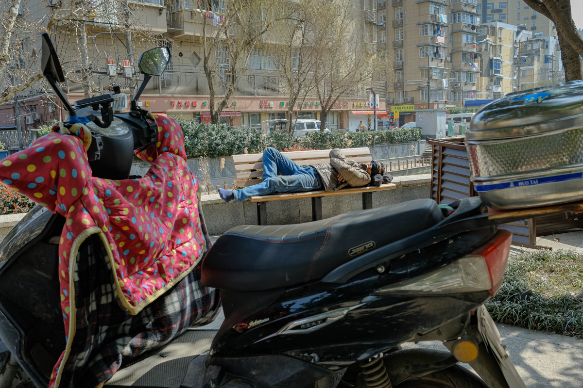 一名外卖员正在路边的长椅上蒙着脸午休.