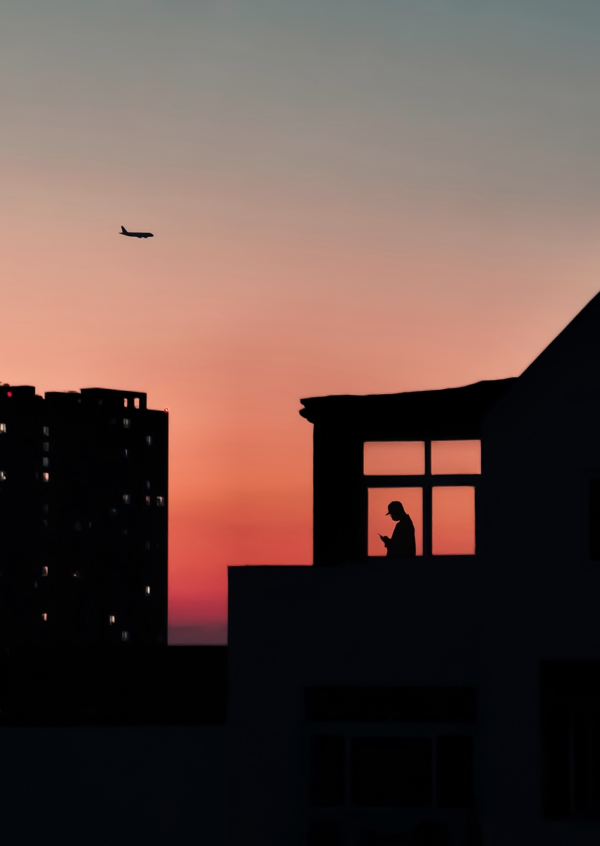 黄昏,一个人静静的看着手机,一架飞机从他的上方飞过