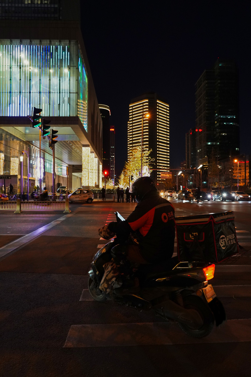 闹市街头,一位快递员在等红灯的同时匆匆拿出手机,盘算着还有几个订单