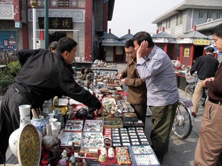 天津鼓楼商业街（北街）北方古玩城，游客们在古玩摊位浏览、选购和讨价还价