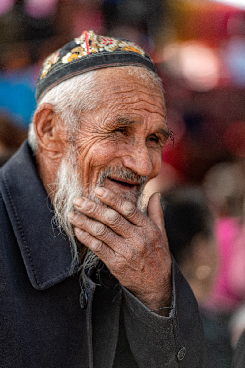 在新疆和田一农贸市场,一位维族老汉与人谈笑风生,看一下捋胡子的手
