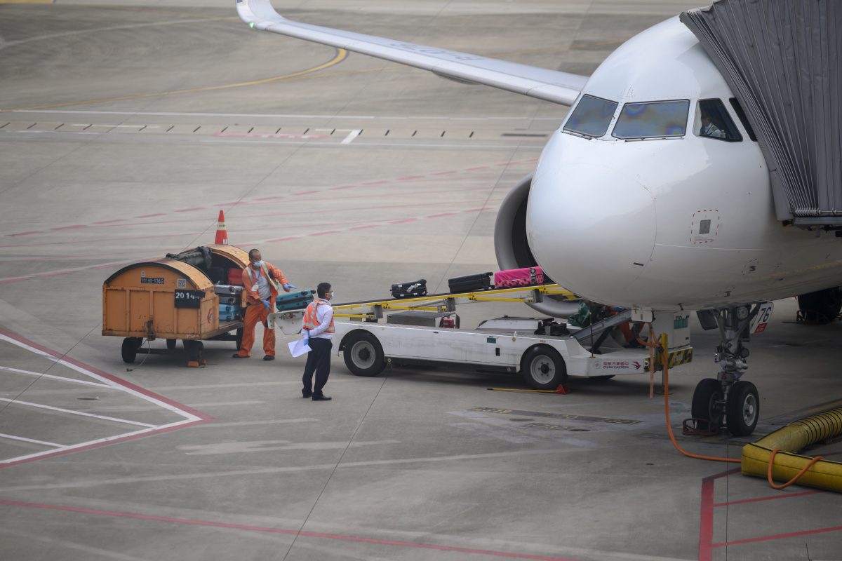 飞机已到达,机场的地勤工作人员们正通过传送带卸行李.