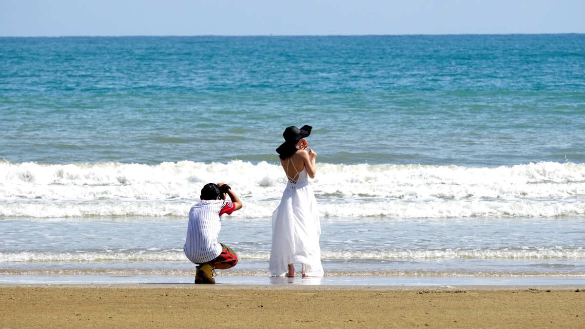 美丽的三亚湾烈日下一对情侣或女青年在拍海边写真佩服佩服