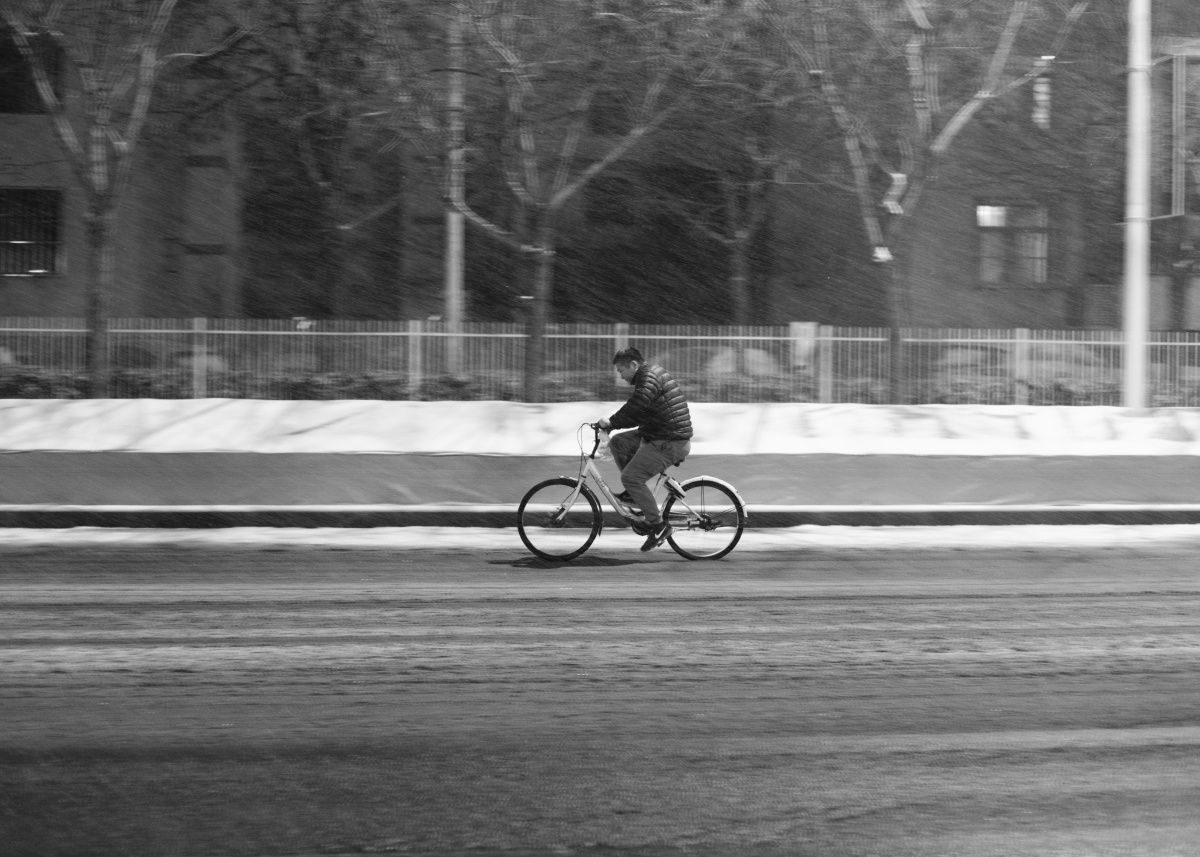 午夜的街头,一位男士顶风冒雪骑行在回家的路上,也许在他