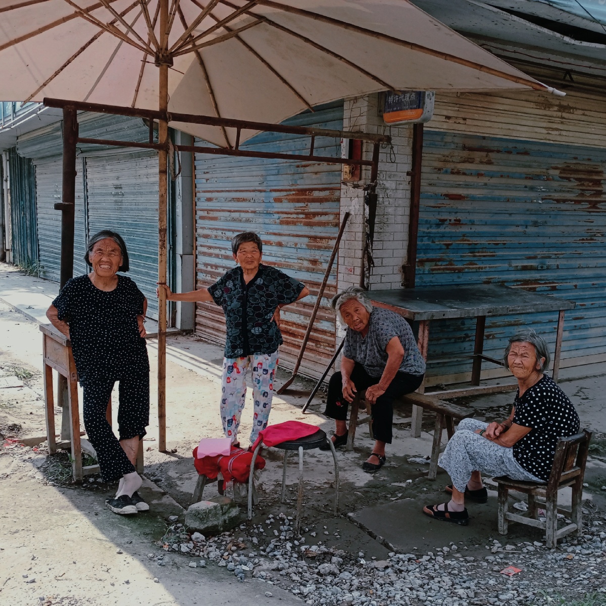 酷暑中,几个老奶奶在街头的伞下闲谈,乘凉.