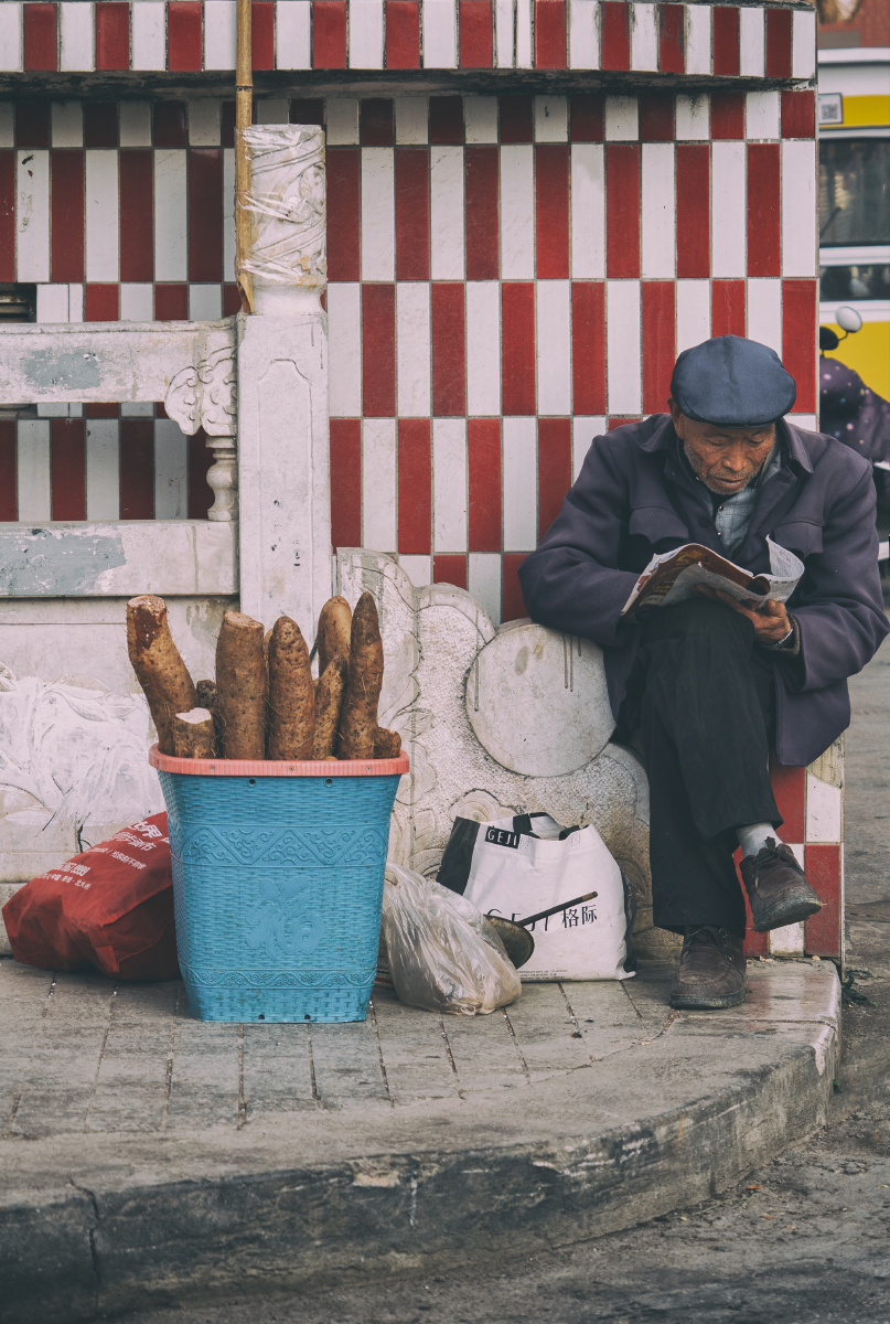 卖菜的老人老人坐在墙边静静地看着书