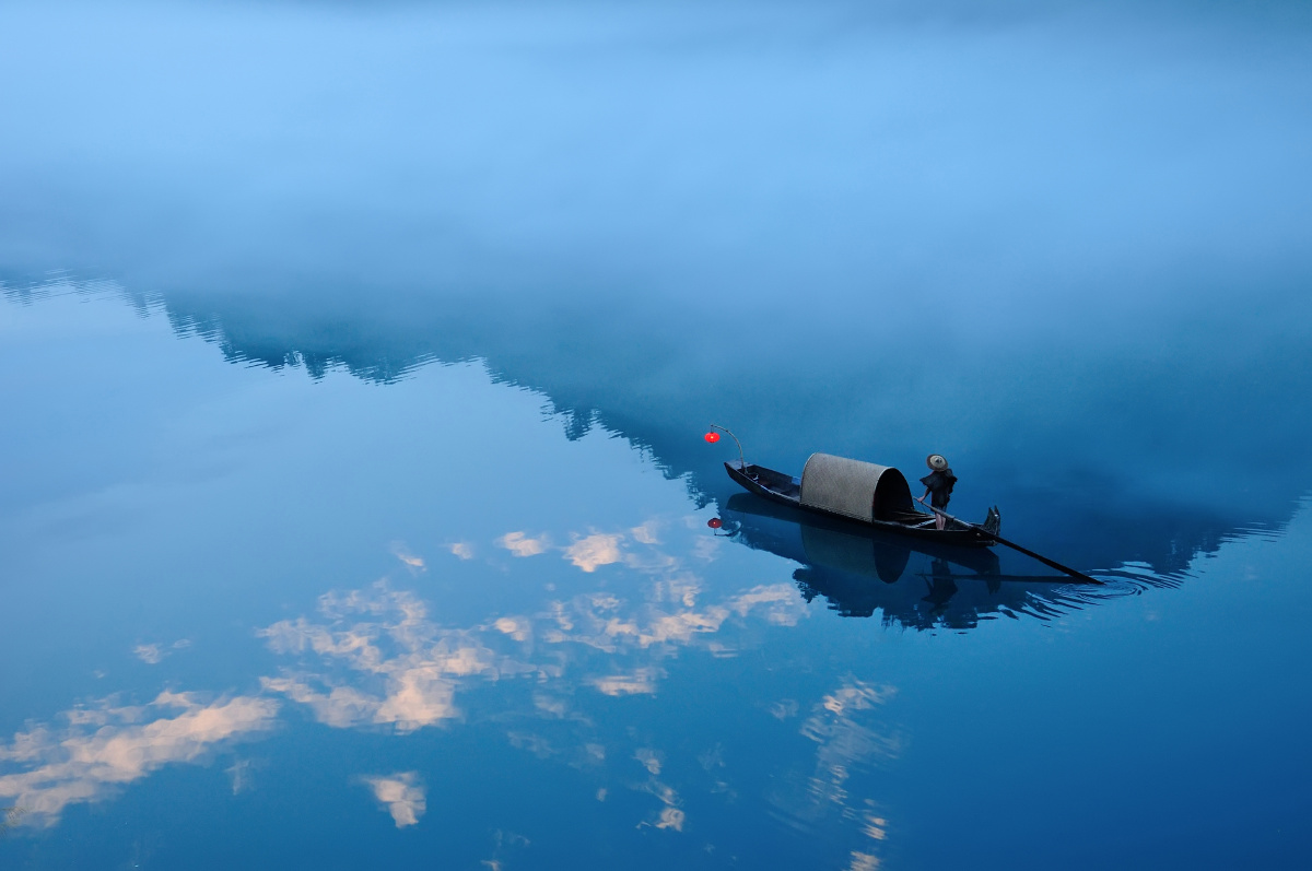 半江迷雾半江云傍晚小船在江面上穿行一半江水倒影着天空一半浓雾遮住